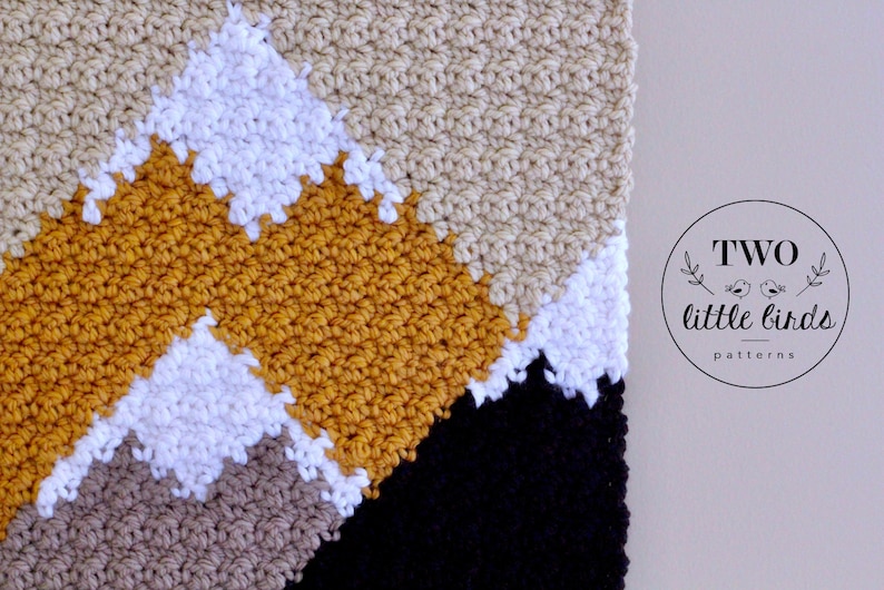 May include: A close-up of a crocheted blanket with a geometric pattern in shades of beige, white, mustard yellow, and black. The blanket is made with a textured stitch and has a modern, minimalist design.