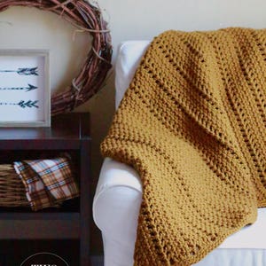 Pu&ograve; includere: Una coperta in crochet color giallo senape drappeggiata su una poltrona bianca. La coperta ha un semplice motivo a punto ed &egrave; realizzata con un filato morbido. La coperta &egrave; un'aggiunta accogliente a qualsiasi soggiorno.