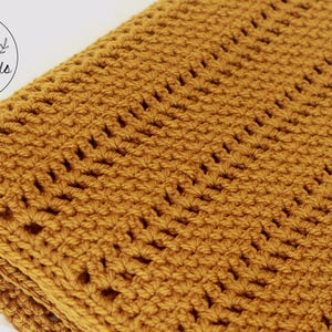 Pu&ograve; includere: Una coperta all'uncinetto color giallo senape con un motivo a punto ripetuto. La coperta &egrave; piegata a met&agrave; e i bordi sono visibili.