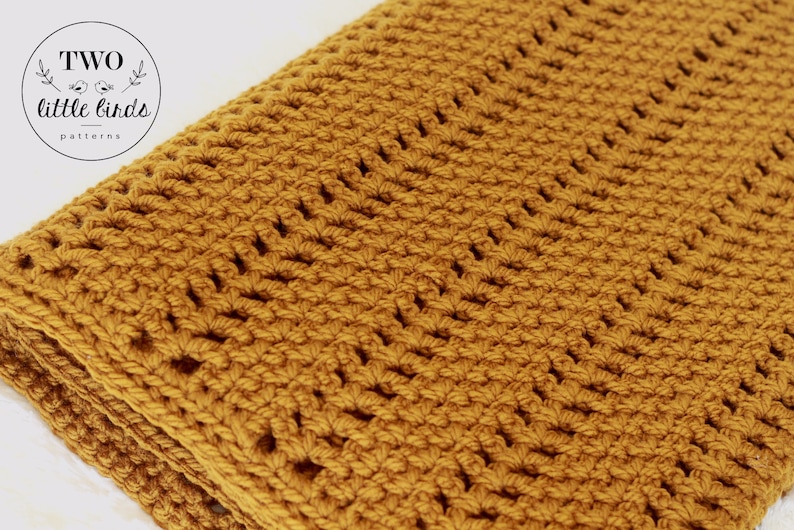 Pu&ograve; includere: Una coperta all'uncinetto color giallo senape con un motivo a punto ripetuto. La coperta &egrave; piegata a met&agrave; e i bordi sono visibili.