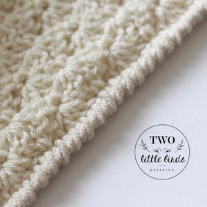 May include: Close-up of a cream-colored crocheted fabric with a textured stitch pattern. The fabric has a finished edge with a decorative border.