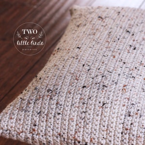May include: A close-up of a beige crocheted cushion with a speckled pattern. The cushion is made with a chunky yarn and has a textured surface.