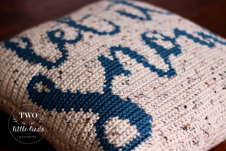 K&ouml;nnte beinhalten: Nahaufnahme eines geh&auml;kelten Kissens mit einem geometrischen Muster in Beige- und T&uuml;rkist&ouml;nen. Das Kissen hat eine strukturierte Oberfl&auml;che und tr&auml;gt ein kleines Logo mit dem Text "TWO little birds patterns".