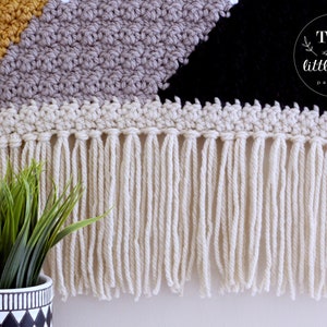 May include: A geometric wall hanging with a black, gray, and yellow pattern. The hanging has a fringe border made of white yarn. The hanging is labeled "TWO little birds patterns".