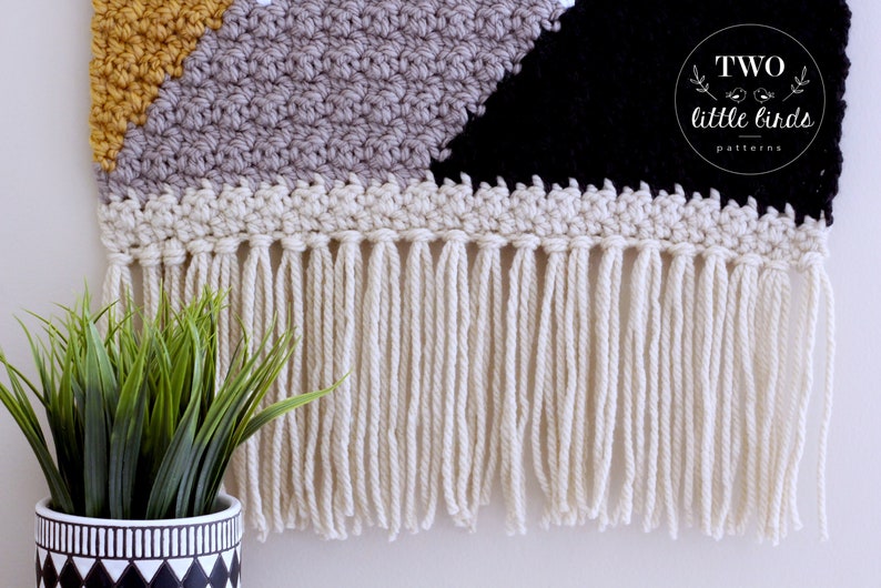 May include: A geometric wall hanging with a black, gray, and yellow pattern. The hanging has a fringe border made of white yarn. The hanging is labeled "TWO little birds patterns".