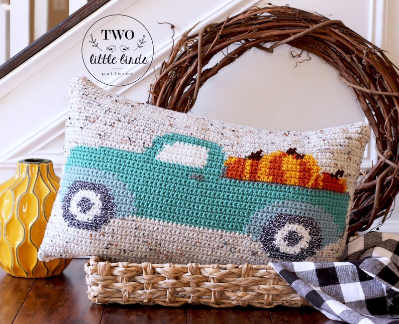 May include: A teal blue crochet cushion featuring a white truck carrying pumpkins. The cushion has a white background with brown speckles. The text "TWO little birds patterns" is on a white circle with a brown border.