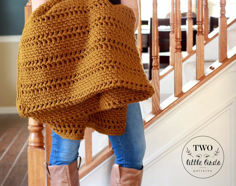 Pu&ograve; includere: Una coperta all'uncinetto color giallo senape con un semplice motivo a punto. La coperta &egrave; tenuta da una persona che indossa jeans blu e stivali marroni. L'immagine include il testo "TWO little birds patterns".