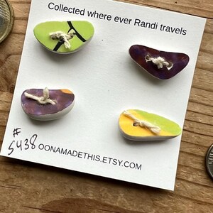 May include: Four colorful ceramic buttons with a white background. The buttons are shaped like a teardrop and have a variety of colors and patterns. The text "Collected where ever Randi travels # 5438 OONAMADETHIS.ETSY.COM" is printed on the white background.