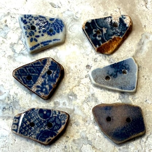 May include: Six irregular, flat ceramic buttons with two holes each. The buttons feature various blue and white patterns, including floral and geometric designs, with visible crackle glaze textures on their surfaces.