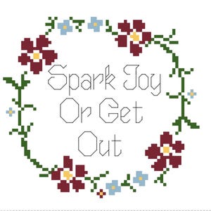 以下が含まれることがあります： 花輪と「Spark Joy Or Get Out」というテキストが書かれたクロスステッチ刺繍のデザインです。