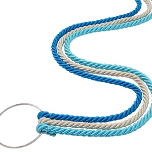 May include: Three twisted ropes in shades of blue and cream are connected to a silver metal ring. The ropes are arranged in a flowing, curved pattern against a white background. The design suggests a nautical or decorative theme.