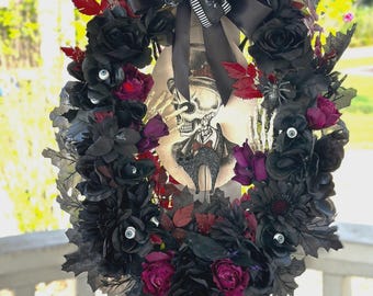 May include: A Halloween wreath with black roses, dark red leaves, and faux eyeballs. A central image features a skeleton in a suit. The wreath is decorated with a black bow and spiderweb accents, creating a spooky, gothic aesthetic.