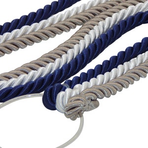 May include: Braided rope in navy blue, white, and tan colors. The rope is twisted and appears to be made of a satin-like material. A silver metal ring is attached to a section of the rope.