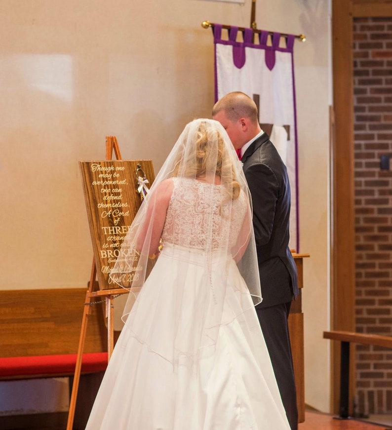 May include: A wooden sign on a tripod easel featuring the text: Though one may be overpowered, two can defend themselves. A Cord of THREE strands is not easily BROKEN. Ecclesiastes 4:12. Michael & Amanda April 7, 2018. The sign has three braided cords.