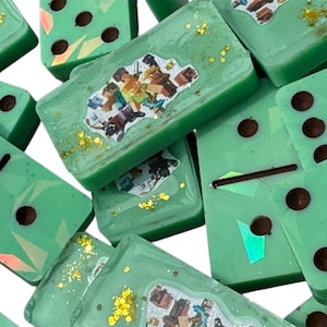 May include: A collection of green dominoes with brown dots and black lines. Some dominoes have a colorful sticker and gold glitter. The dominoes are scattered, showing their various sides.