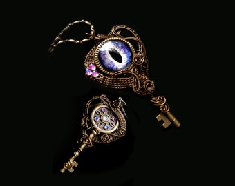 Puede incluir: Dos colgantes en forma de llave adornados con un diseño de ojo azul y morado con un centro de cristal. Los colgantes están hechos de alambre y tienen un acabado bronce.