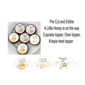 May include: Edible cupcake toppers with a bee theme. The toppers are round and feature illustrations of bees, honey pots, and the text "A Little Honey is on the way" and "Mommy to Bee". The toppers are pre-cut and edible.