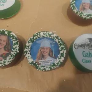 May include: Chocolate-covered cookies with graduation-themed decorations. Each cookie features a photo of a graduate, surrounded by green and white sprinkles. Some cookies have text that says "Congratulations" and the graduate's name.