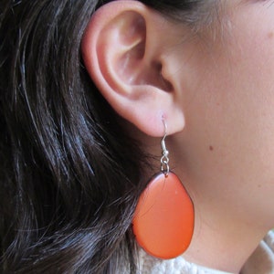 May include: A pair of orange, oval-shaped earrings with silver hooks.