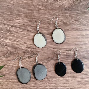 May include: Four pairs of earrings with silver hooks and oval-shaped pendants. Two pairs have black and white oval pendants, and two pairs have black and gray oval pendants.