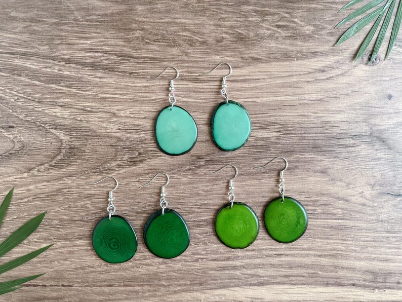May include: A set of six earrings featuring green and teal wood slices with silver hooks. The earrings are arranged in two rows of three.