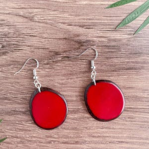 May include: A pair of red and black resin earrings with silver hooks. The earrings are oval shaped and have a smooth, glossy finish.