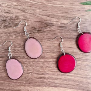 May include: Three pairs of earrings with a wood-like design. The earrings are made of resin and have a pink, red, and light pink color.