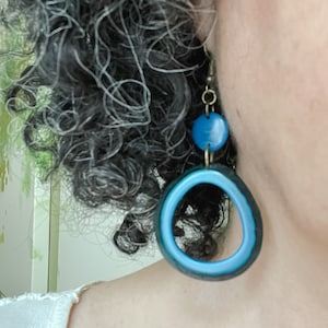 May include: Blue and black resin hoop earrings with a smaller blue circle charm hanging from the bottom.