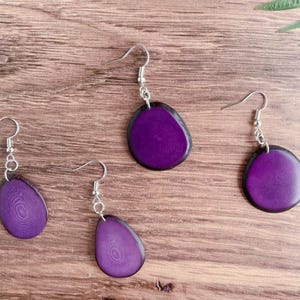 May include: Three pairs of purple resin earrings with silver hooks. The earrings are shaped like a teardrop and have a wood grain pattern.