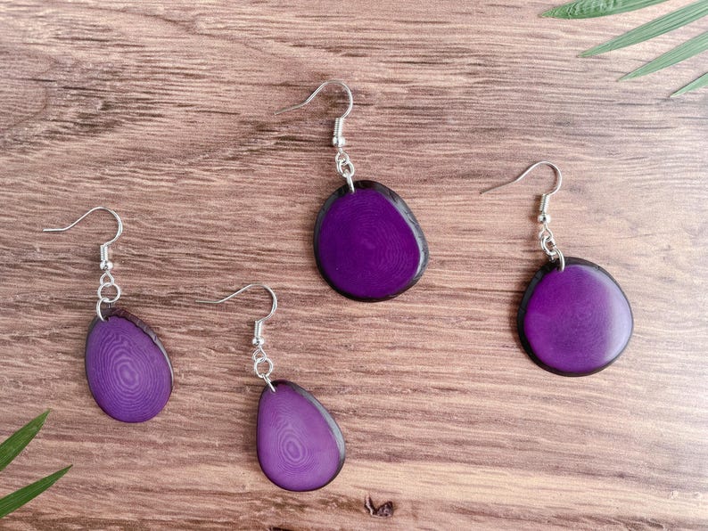 May include: Three pairs of purple resin earrings with silver hooks. The earrings are shaped like a teardrop and have a wood grain pattern.