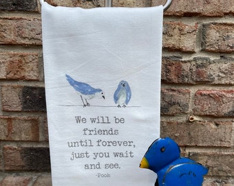 May include: A white kitchen towel with a blue bird design and the quote "We will be friends until forever, just you wait and see. -Pooh".