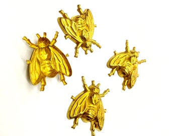 May include: Four gold-colored metal bee-shaped ornaments or buttons. Each piece features a detailed, embossed insect design with wings, a segmented body, and six legs. The metallic finish is reflective and uniform across all four individual items.