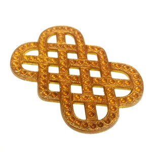 May include: A gold-colored metal embellishment featuring an intricate, repeating interlaced knot pattern. The surface of the flat, geometric shape is textured with a series of small, raised circular dots that follow the entire length of the design.
