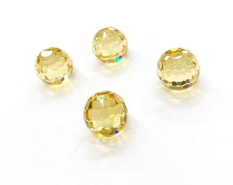 Puede incluir: Cuatro cuentas redondas facetadas de un color amarillo dorado translúcido. Cada cuenta presenta una superficie geométrica de múltiples facetas que refleja la luz, creando pequeños reflejos prismáticos sobre las formas esféricas en blanco.