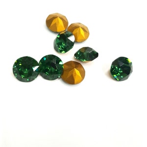 May include: A collection of round, faceted gemstones in deep emerald green and matte gold. The green stones feature a brilliant, reflective cut, while the gold stones have a smooth, opaque finish. These small, circular decorative items are arranged.