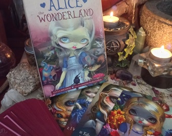 May include: An "Alice in Wonderland" oracle deck with a book and several cards. The book cover features a doll-like illustration of Alice in a blue dress. The cards have similar artwork. The text on the book reads "Alice the Wonderland oracle".