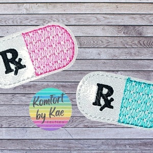 May include: Two embroidered pill-shaped patches with a white background and a black "Rx" symbol. One patch has a pink half and the other has a turquoise half.