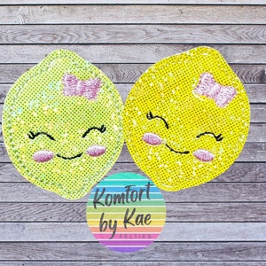 May include: Two yellow felt lemon appliques with pink bows and smiling faces. The lemons are on a woodgrain background with a circular logo that says "Komfort by Kae Felties".