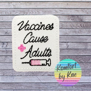 May include: White felt patch with black embroidery that reads "Vaccines Cause Adults" with a pink plus sign and a black and pink syringe.