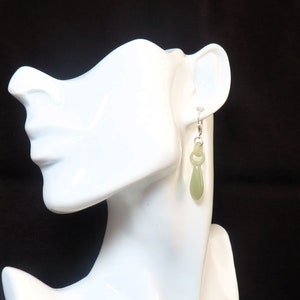 May include: A pair of dangle earrings with a light green jade stone pendant. The earrings are silver and have a simple design.