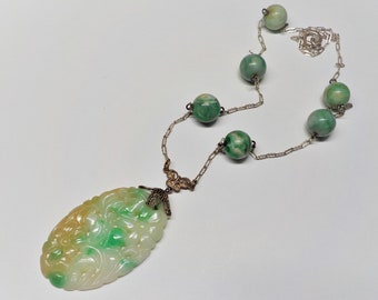 May include: A green jade necklace with a carved pendant and round beads. The necklace is made of silver and has a delicate chain.