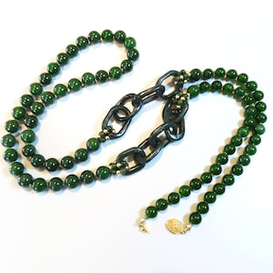 May include: A long green jade necklace with a large dark green jade chain link pendant. The necklace is made of round beads and has a gold clasp.