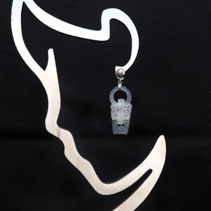 May include: A white, ornate, silver-toned earring with a delicate design. The earring is hanging from a silver hook.