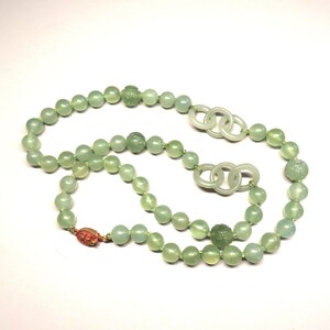 May include: A green jade necklace with carved beads and a double ring pendant. The necklace is strung on a thin cord and has a gold clasp.