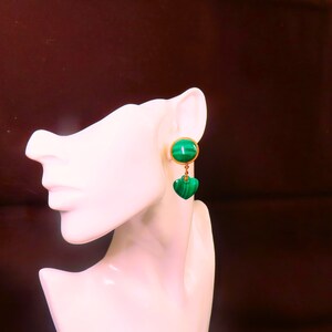 May include: A pair of green malachite drop earrings with gold accents. The earrings feature a round malachite stone at the top and a heart-shaped malachite stone dangling below.