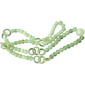 May include: A green jade necklace with round beads and a larger round bead at the end. The necklace has a chain of connected jade rings.