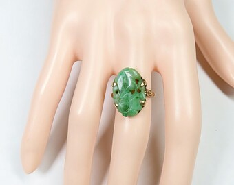 May include: A green jade ring with a carved floral design set in a gold band.