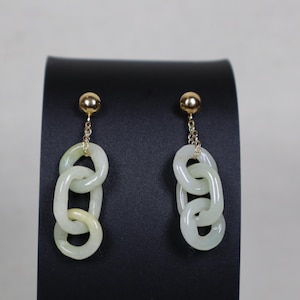 Puede incluir: Un par de pendientes colgantes con postes dorados en forma de bola conectados por cadenas cortas a eslabones de piedra verde pálido translúcida. Cada pendiente consta de tres anillos de piedra ovalados entrelazados que cuelgan verticalmente.