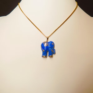 May include: A gold chain necklace with a blue lapis lazuli elephant pendant. The elephant has gold accents and a small red stone on its trunk.