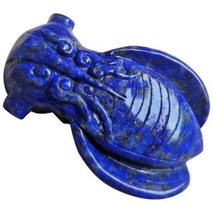 Op de afbeelding: Een blauwe lapis lazuli-carving van een cicada-insect. De carving is gedetailleerd en ingewikkeld, met een gladde, gepolijste afwerking.